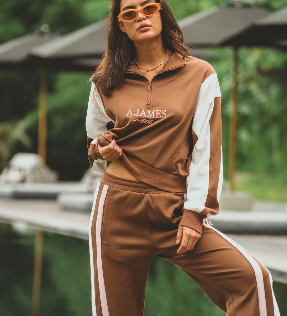 Woman wearing a brown and white tracksuit with 'AJAMES' branding outdoors.