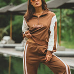 Woman wearing a brown and white tracksuit with 'AJAMES' branding outdoors.