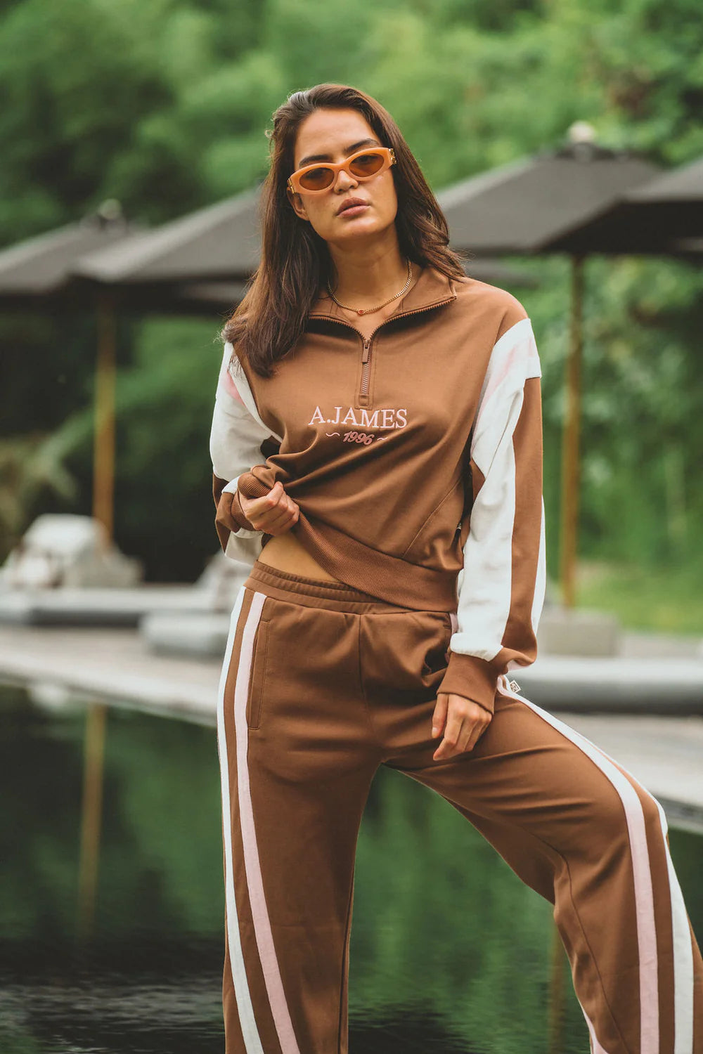 Woman wearing a brown and white tracksuit with 'AJAMES' branding outdoors.