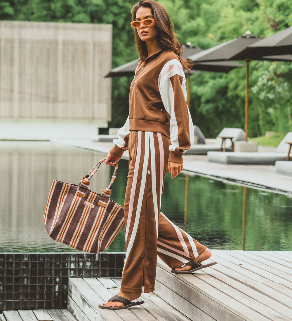 Woman in a brown outfit with white stripes standing by a poolside.