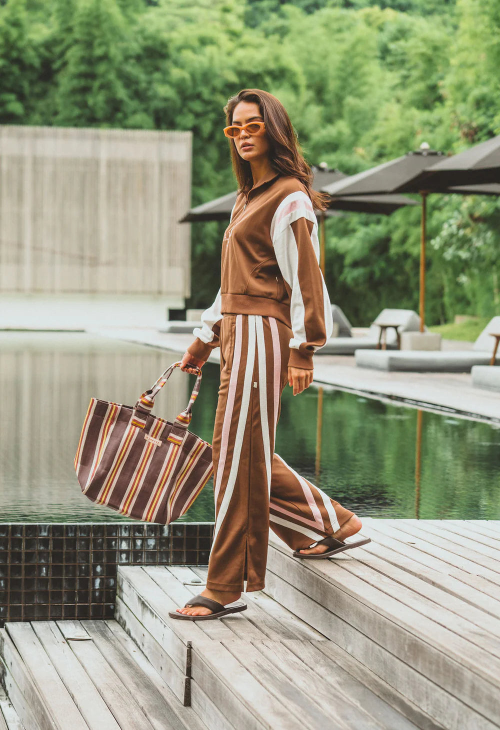 Woman in a brown outfit with white stripes standing by a poolside.