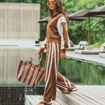 Woman in a brown outfit with white stripes standing by a poolside.