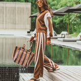 Woman in a brown outfit with white stripes standing by a poolside.