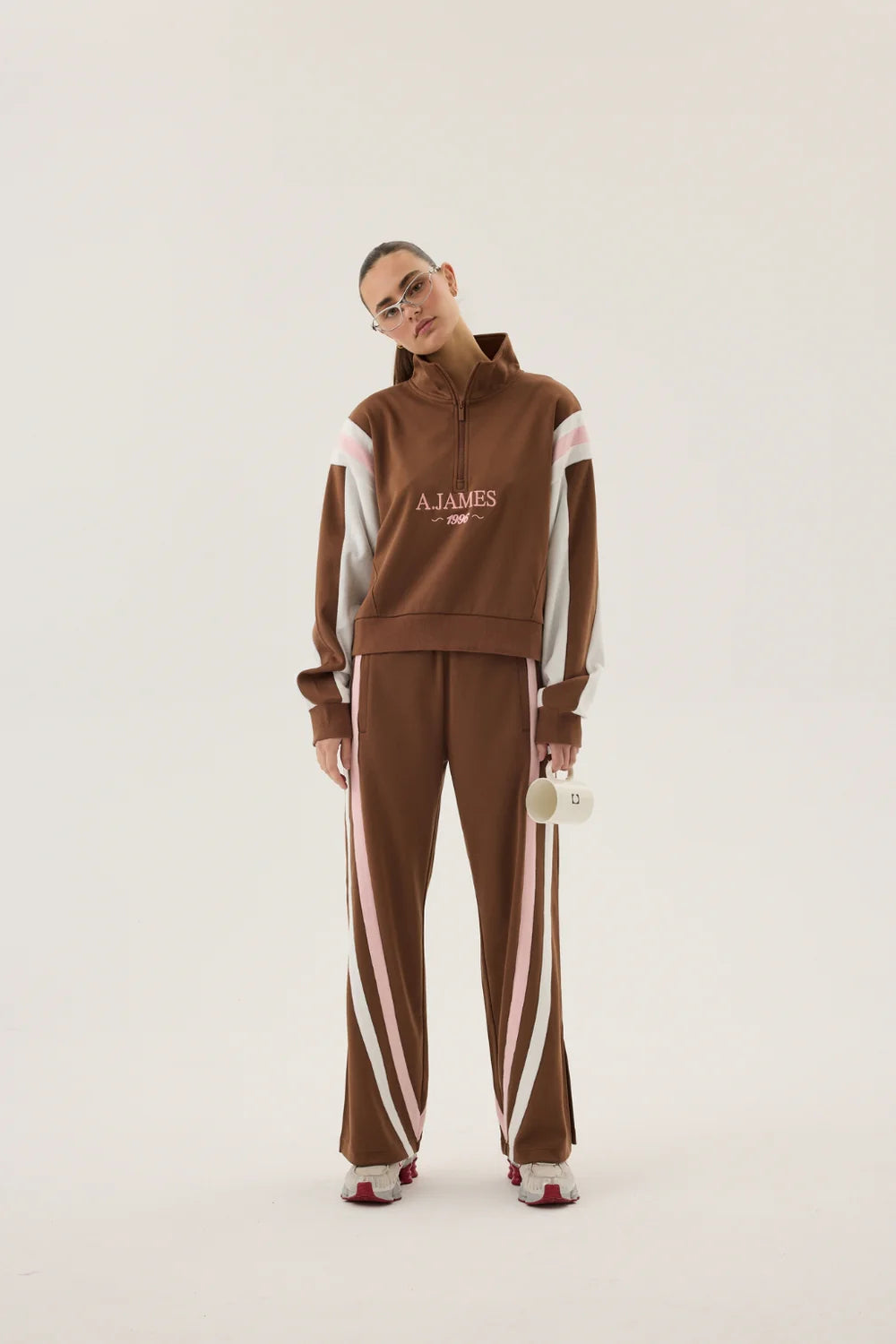 Person wearing a brown tracksuit with white stripes and 'AJames' branding on a beige background