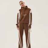 Person wearing a brown tracksuit with white stripes and 'AJames' branding on a beige background