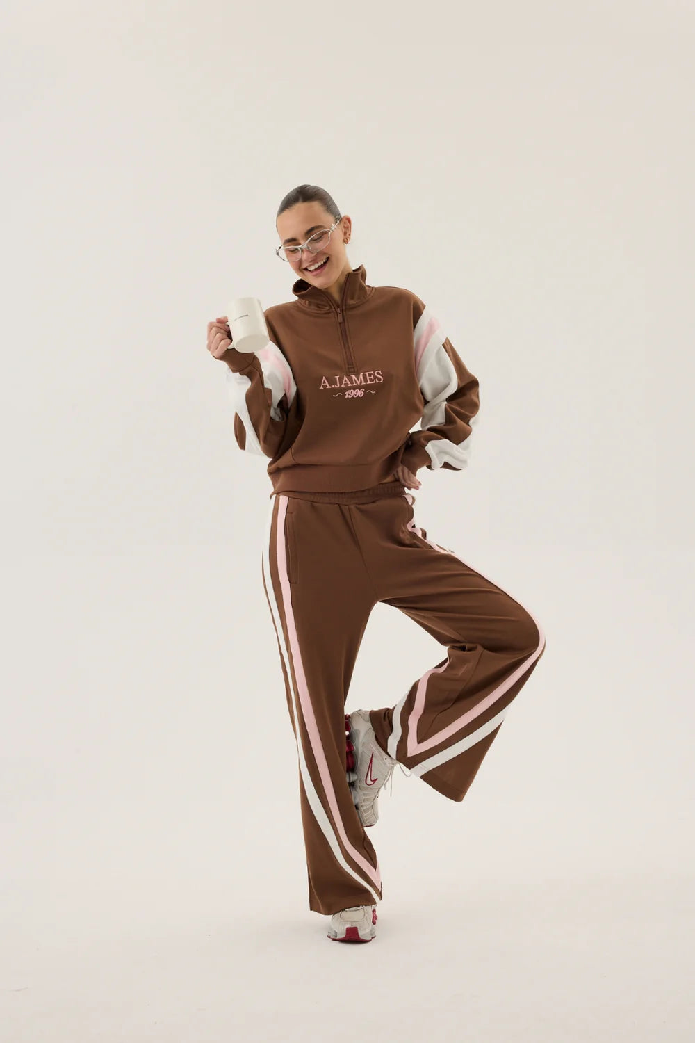 Person wearing a brown tracksuit with white stripes on a white background