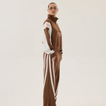 Person wearing a brown tracksuit with white stripes on a plain background