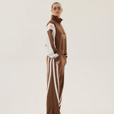 Person wearing a brown tracksuit with white stripes on a plain background