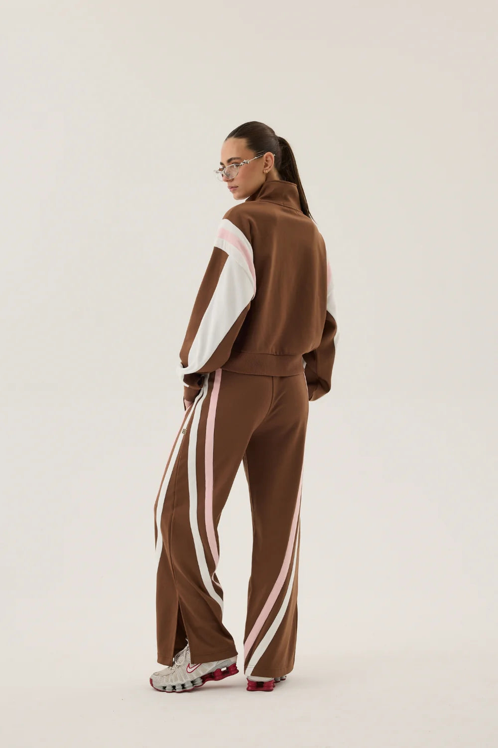 Person wearing a brown tracksuit with white stripes on a plain background