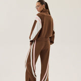 Person wearing a brown tracksuit with white stripes on a plain background