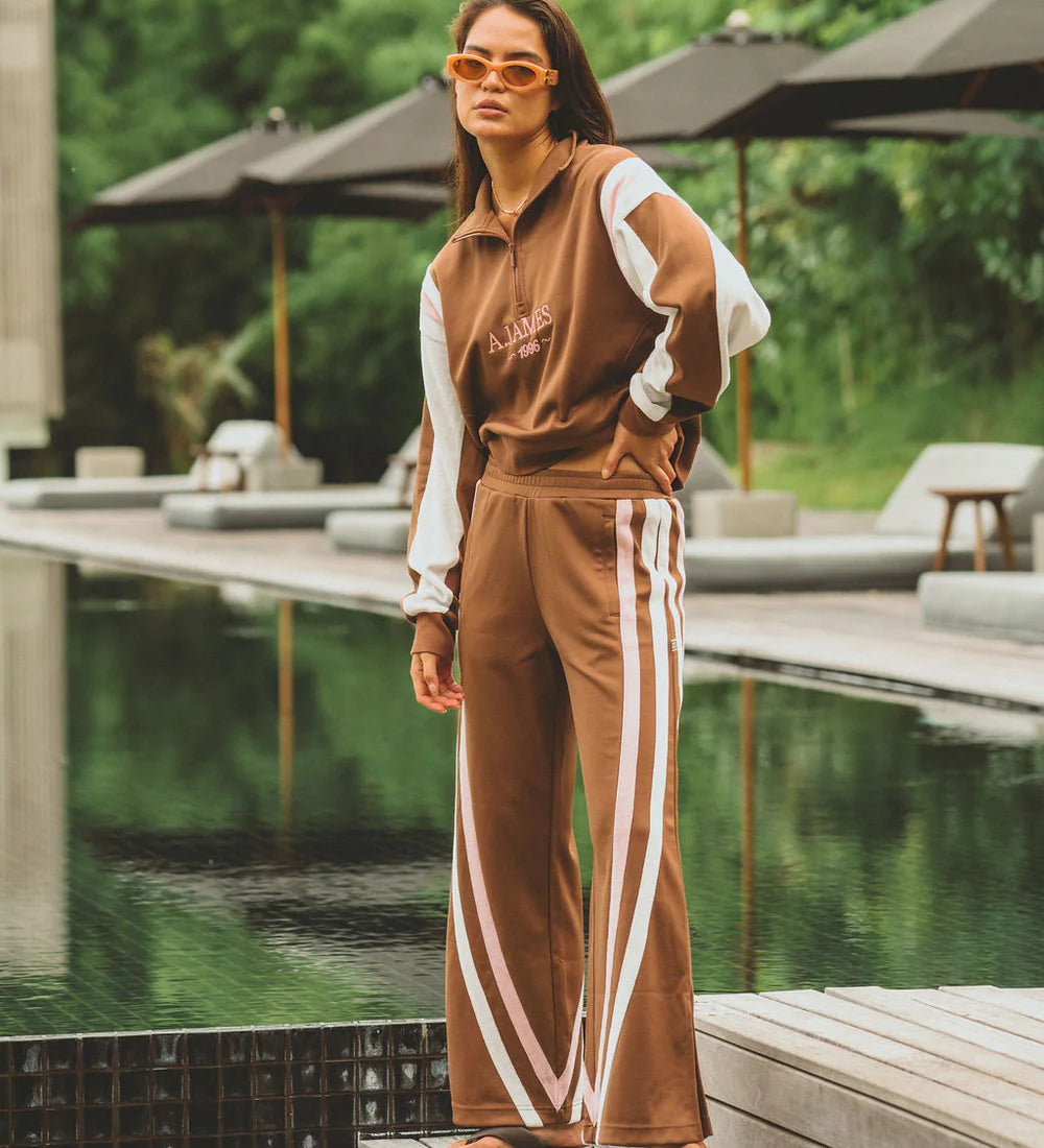 Woman in a brown tracksuit with white stripes standing by a poolside.