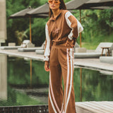 Woman in a brown tracksuit with white stripes standing by a poolside.