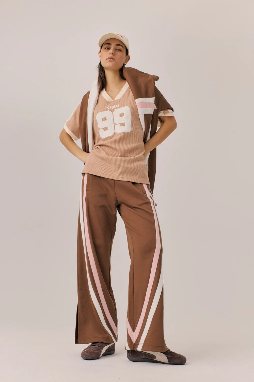 Person wearing a brown and white outfit with a cap on a plain background