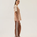 Woman wearing a beige top and brown pants with white stripes on a plain background