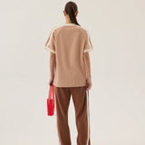 Person wearing a beige top and brown pants with white stripes, holding a red bag on a plain background