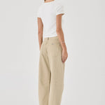 Woman wearing beige pants and a white top on a plain background