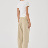 Woman wearing beige pants and a white top on a plain background