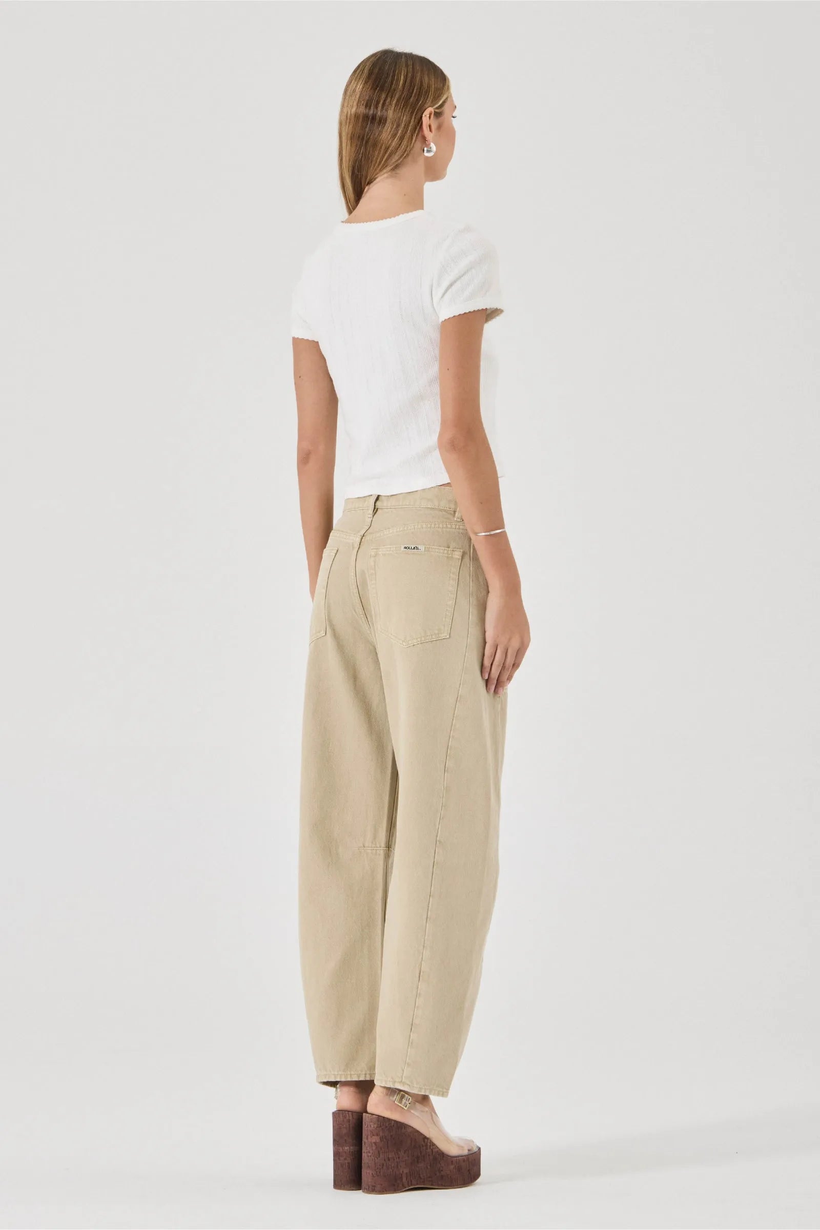 Woman wearing beige pants and a white top on a plain background