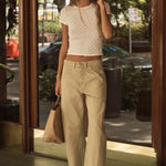 Woman in a white top and beige pants standing outside a building, talking on a phone.