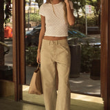 Woman in a white top and beige pants standing outside a building, talking on a phone.