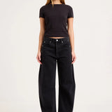 A woman modeling a black short-sleeve crop top and black wide-leg jeans against a plain light gray studio background.