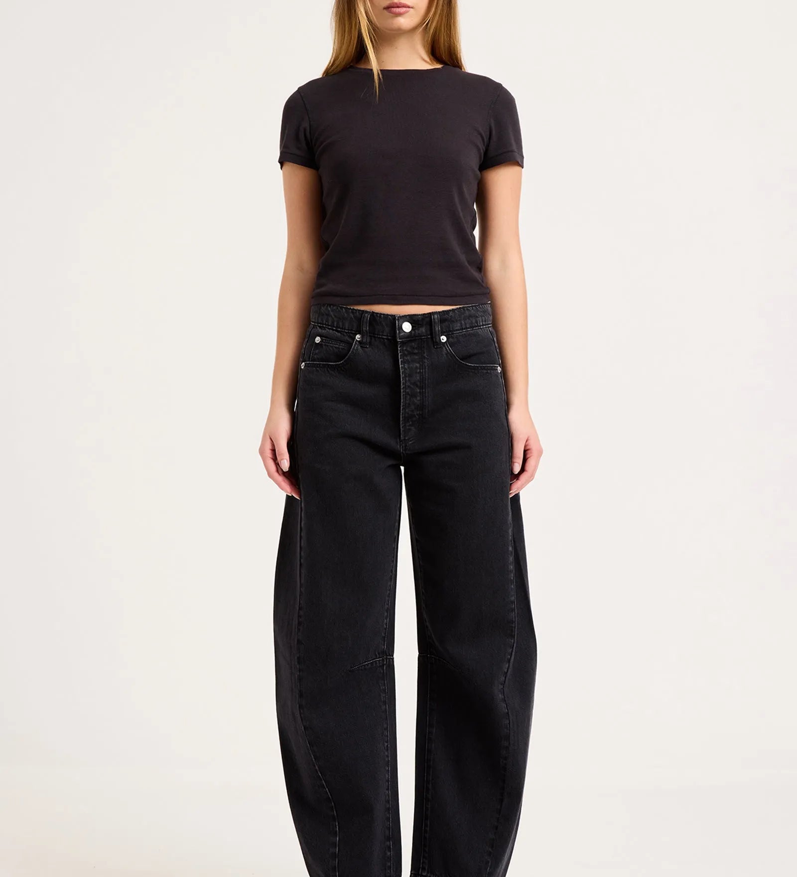 A woman modeling a black short-sleeve crop top and black wide-leg jeans against a plain light gray studio background.