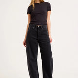 A woman modeling a black short-sleeve crewneck t-shirt and black wide-leg jeans against a plain white studio background.