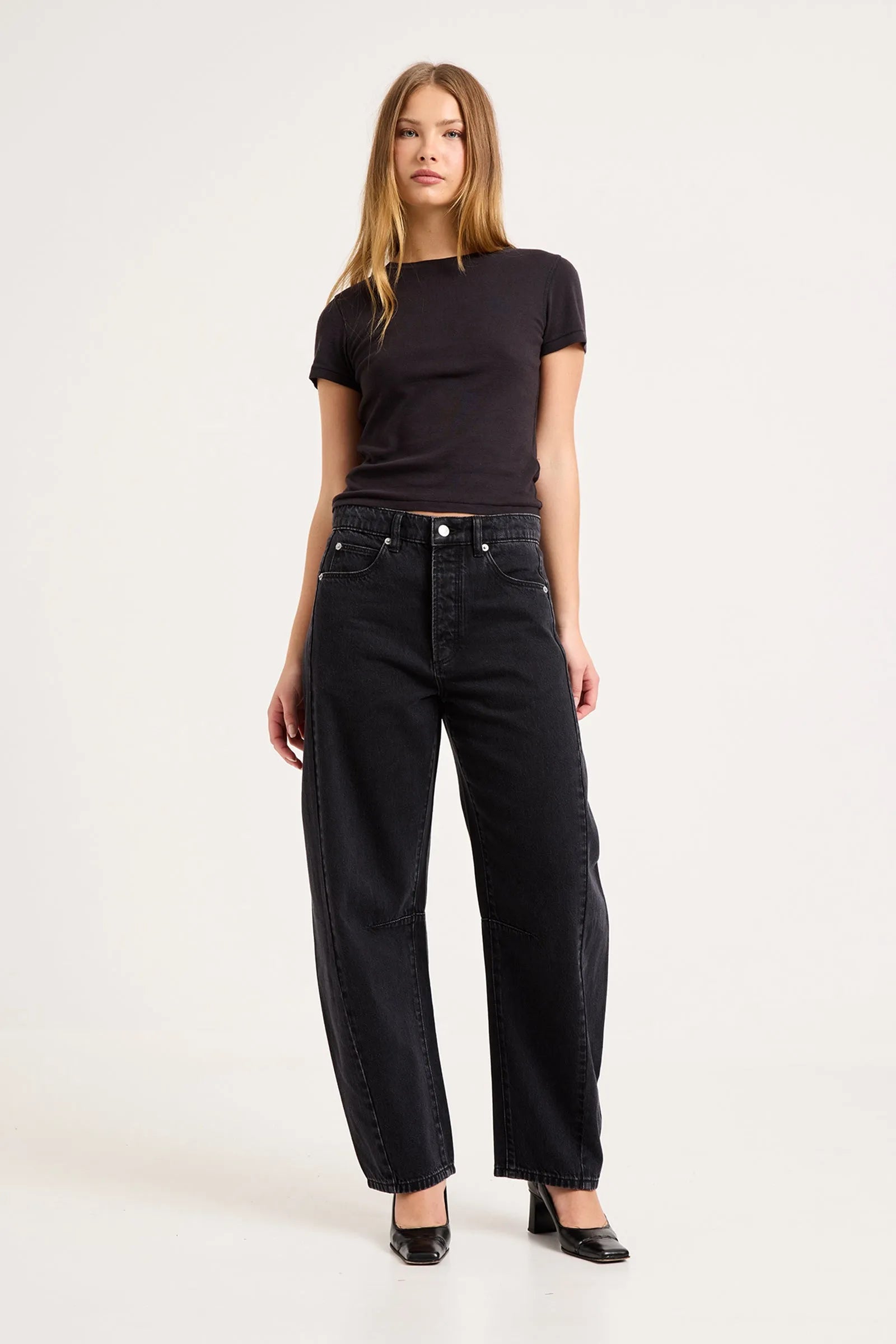 A woman modeling a black short-sleeve crewneck t-shirt and black wide-leg jeans against a plain white studio background.