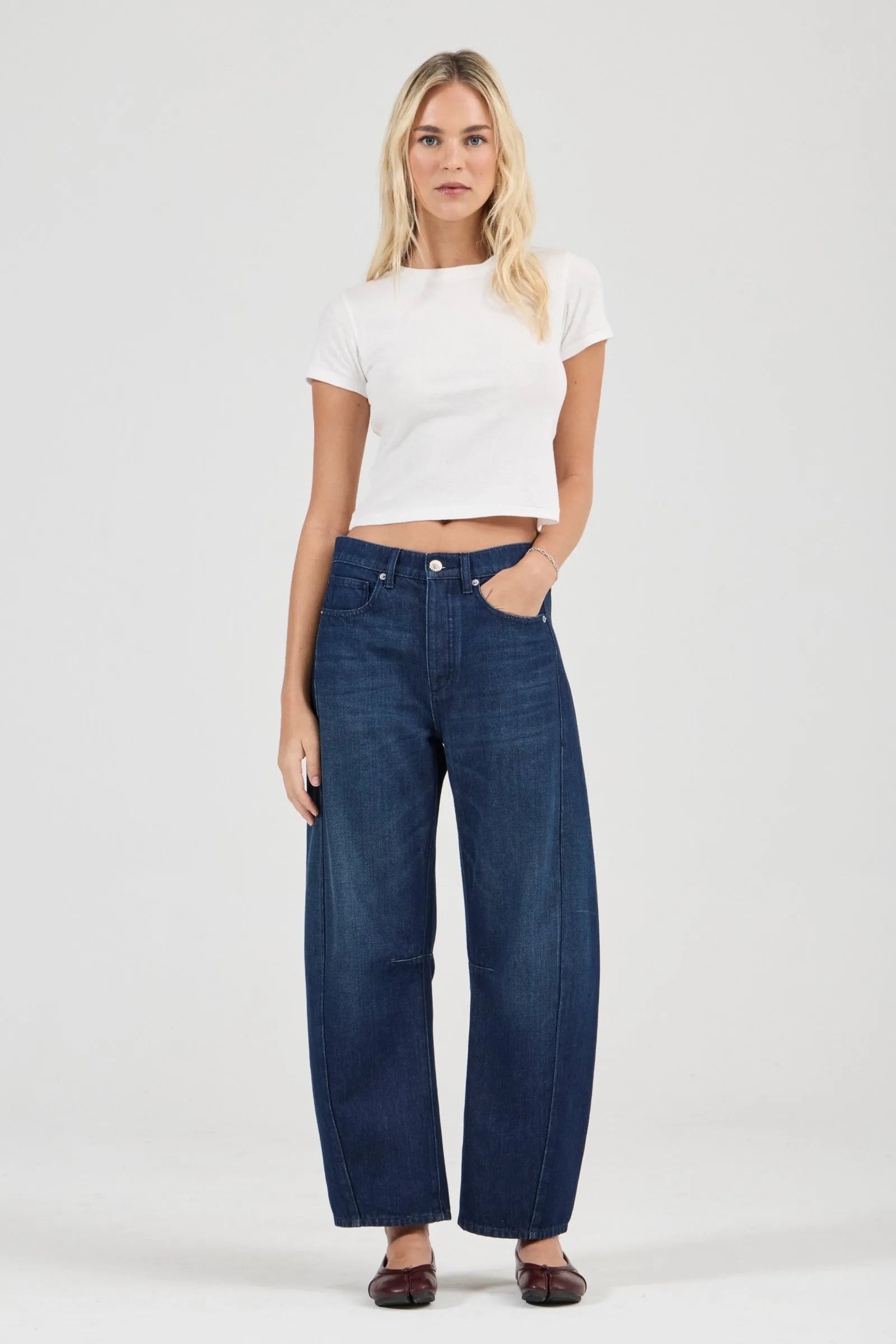 Woman wearing a white crop top and blue jeans on a white background