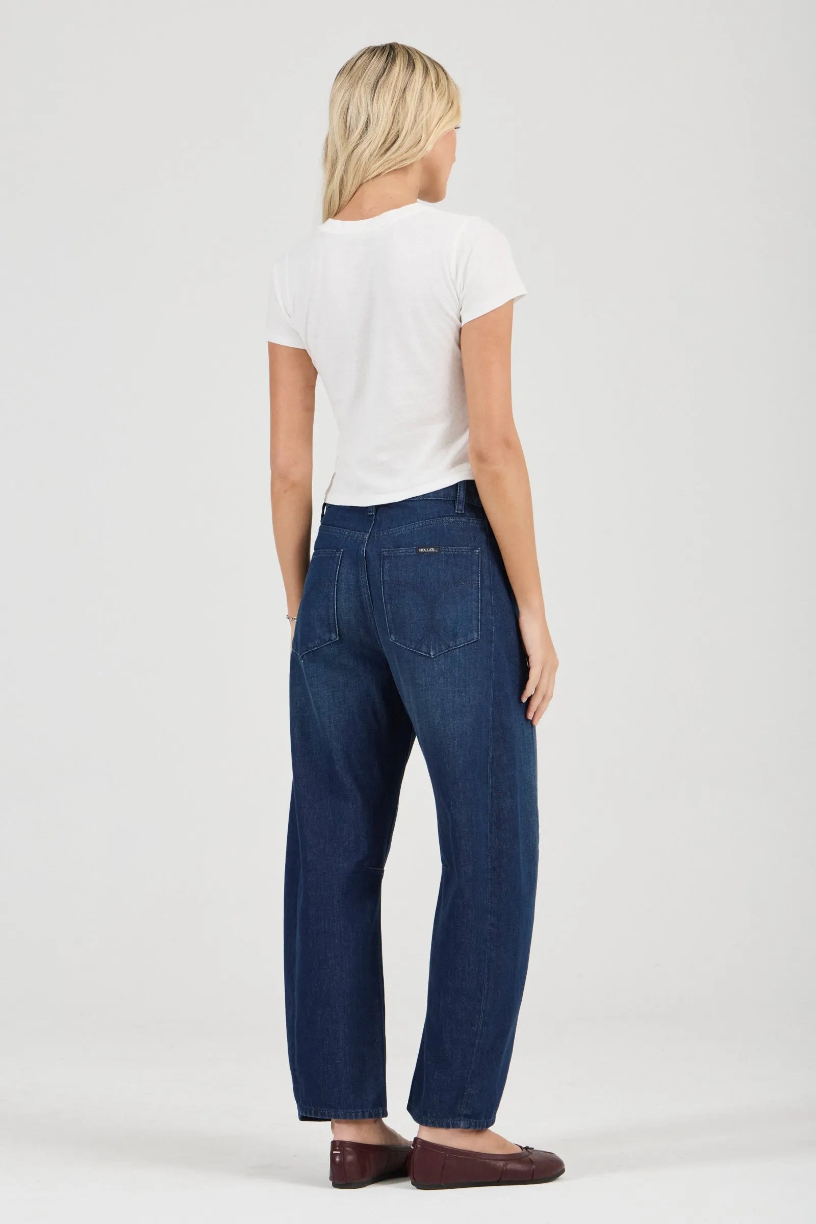 Woman wearing blue jeans and a white t-shirt on a plain background