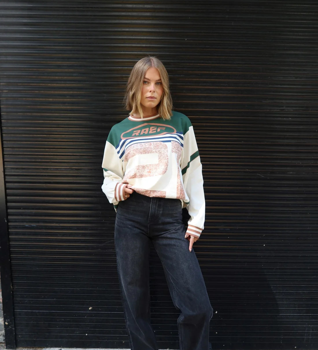 Person wearing a Printed Long sleeve Jersey and dark jeans standing against a black metal shutter.