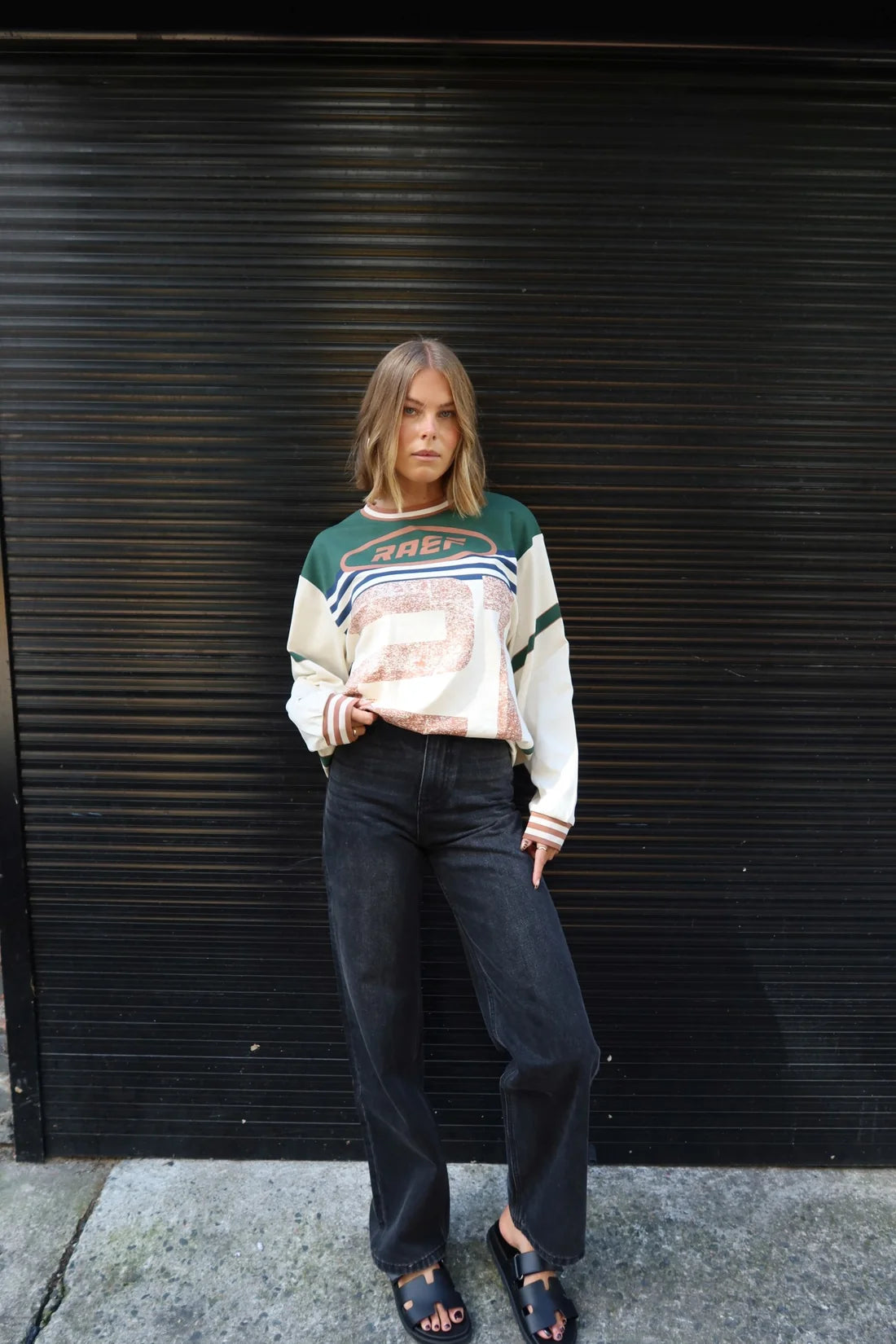 Person wearing a Printed Long sleeve Jersey and dark jeans standing against a black metal shutter.