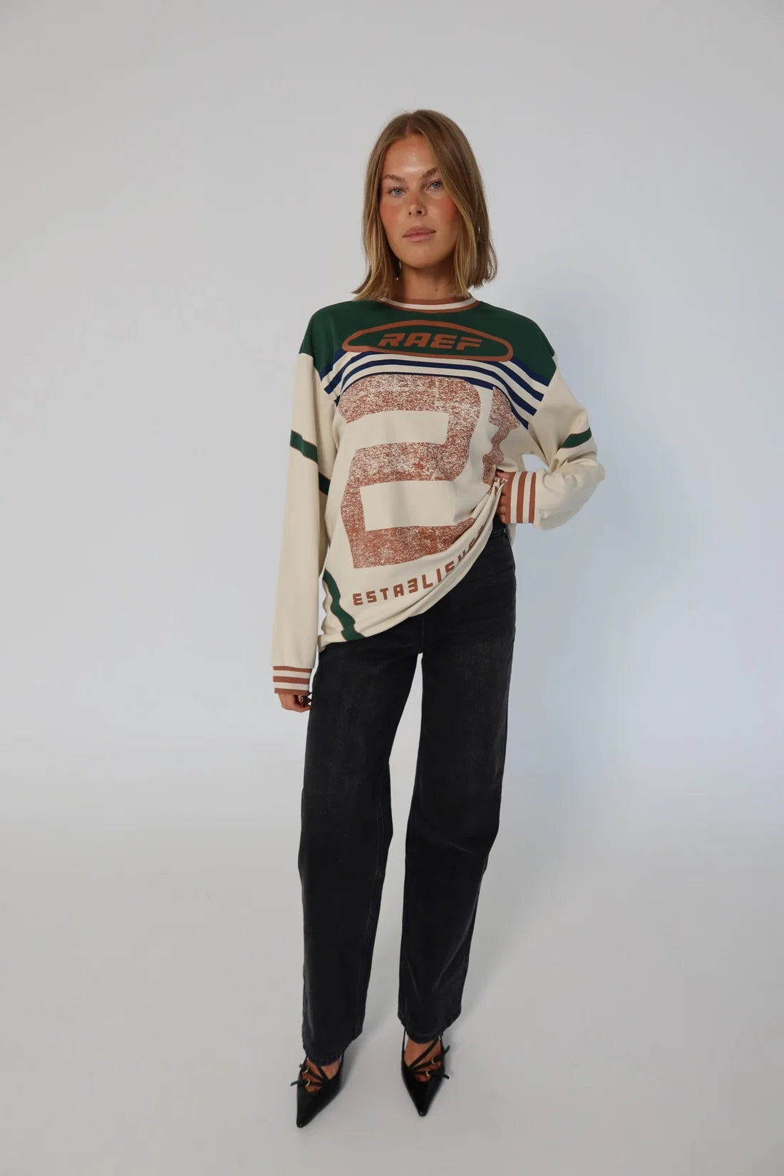 Woman wearing a patterned sweater and black pants on a white background