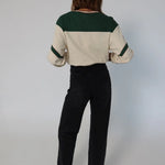 Person wearing a cream and green color-blocked top with black pants on a plain background