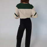 Person wearing a cream and green color-blocked top with black pants on a plain background