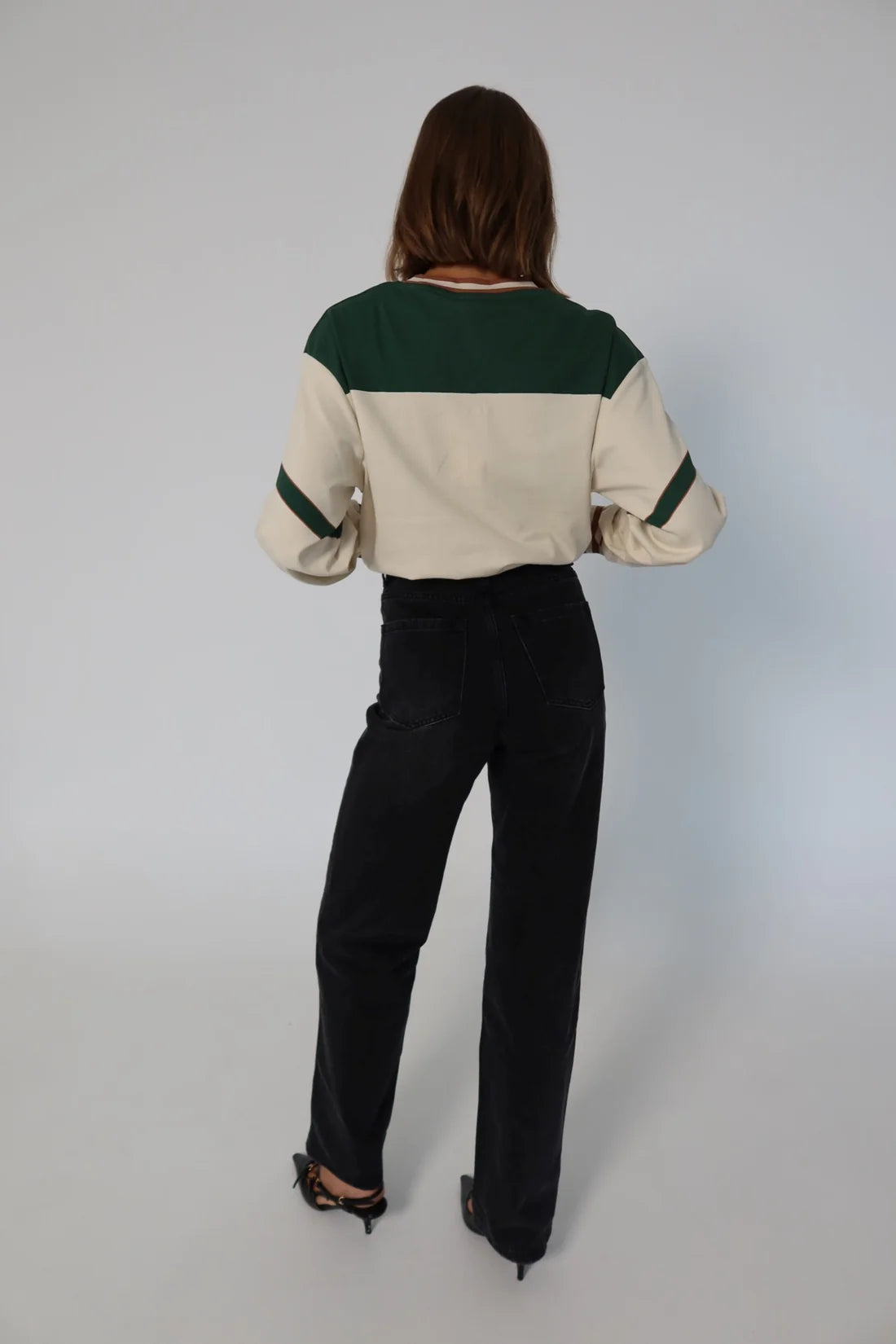 Person wearing a cream and green color-blocked top with black pants on a plain background