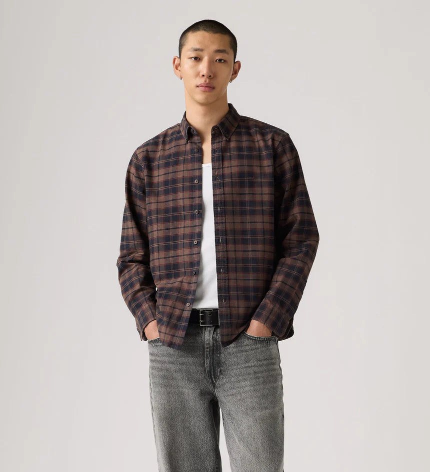 Man wearing a plaid shirt over a white t-shirt with gray jeans on a plain background