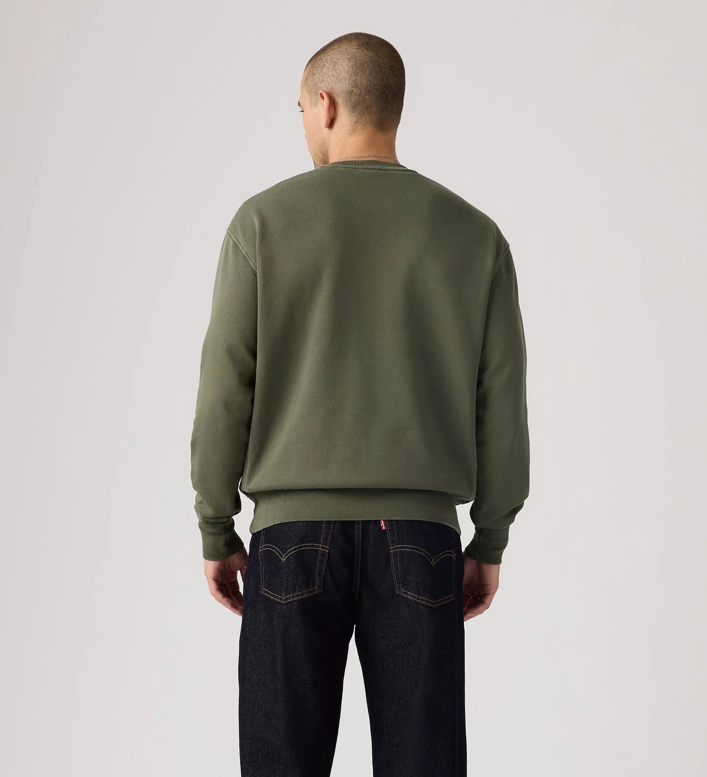 Person wearing a green sweatshirt and dark jeans on a light gray background