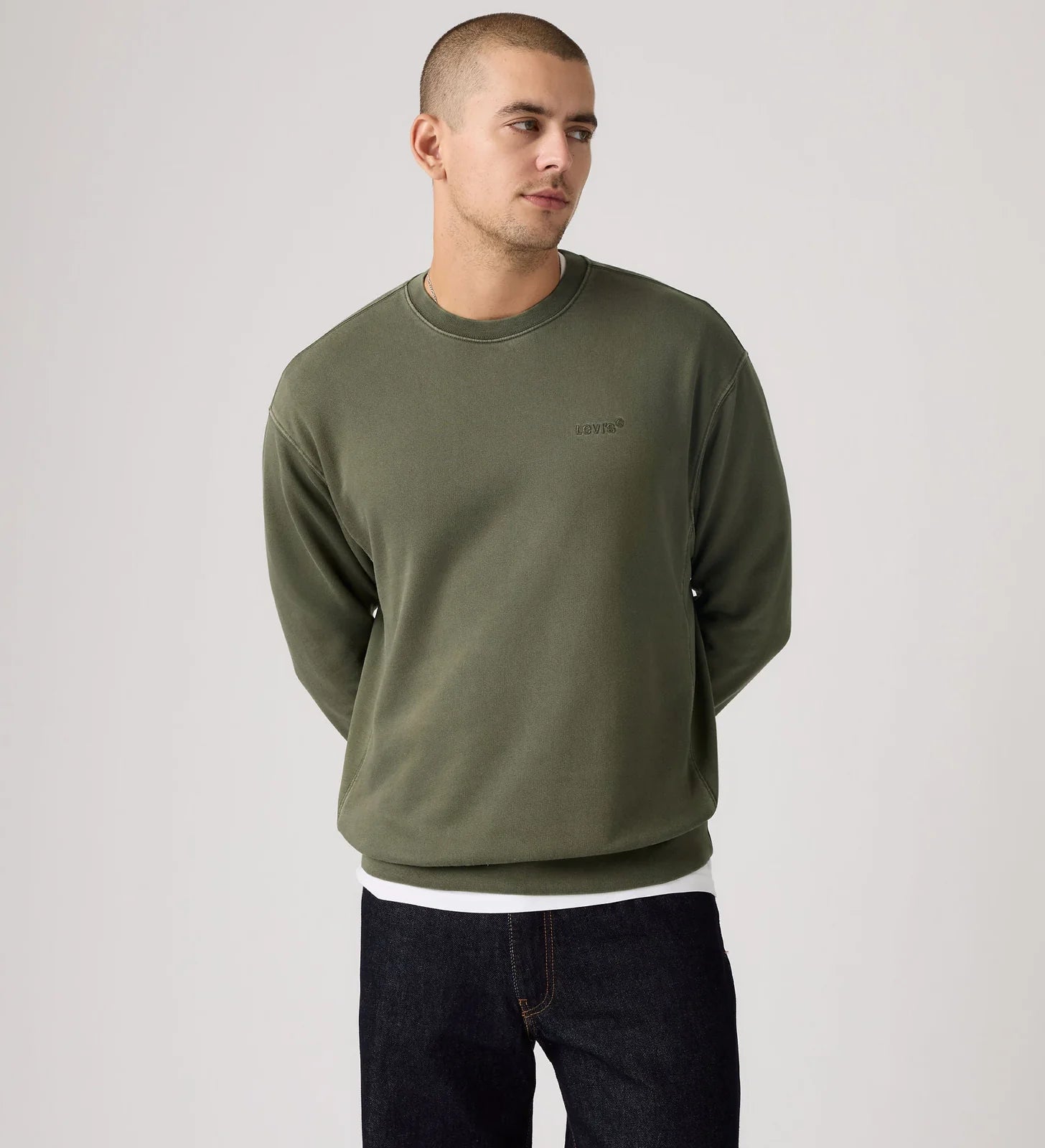Man wearing an olive green sweatshirt with a brand logo on a light gray background