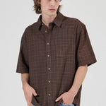 Man wearing a brown plaid shirt and blue jeans against a white background