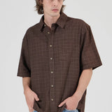 Man wearing a brown plaid shirt and blue jeans against a white background