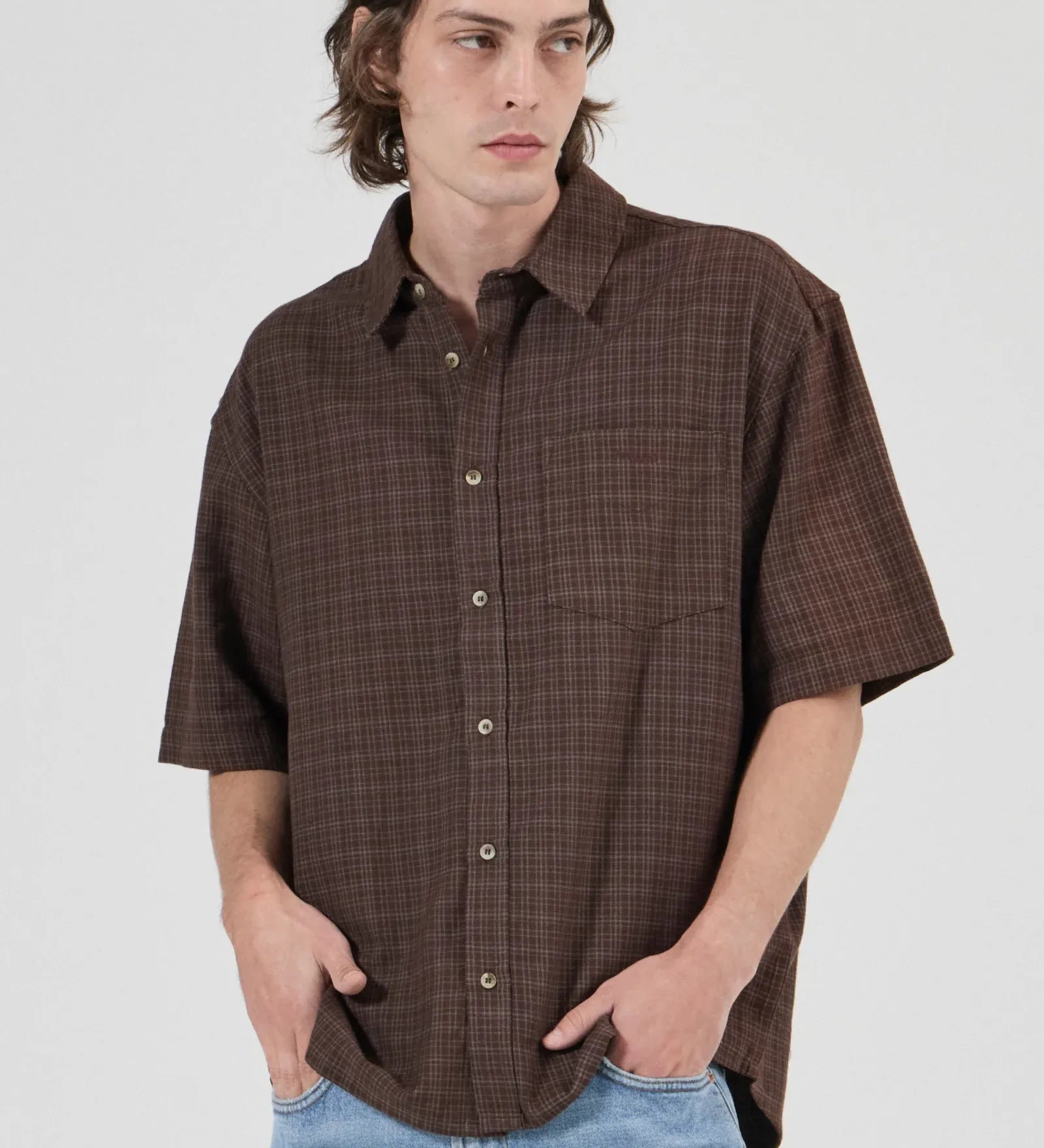 Man wearing a brown plaid shirt and blue jeans against a white background