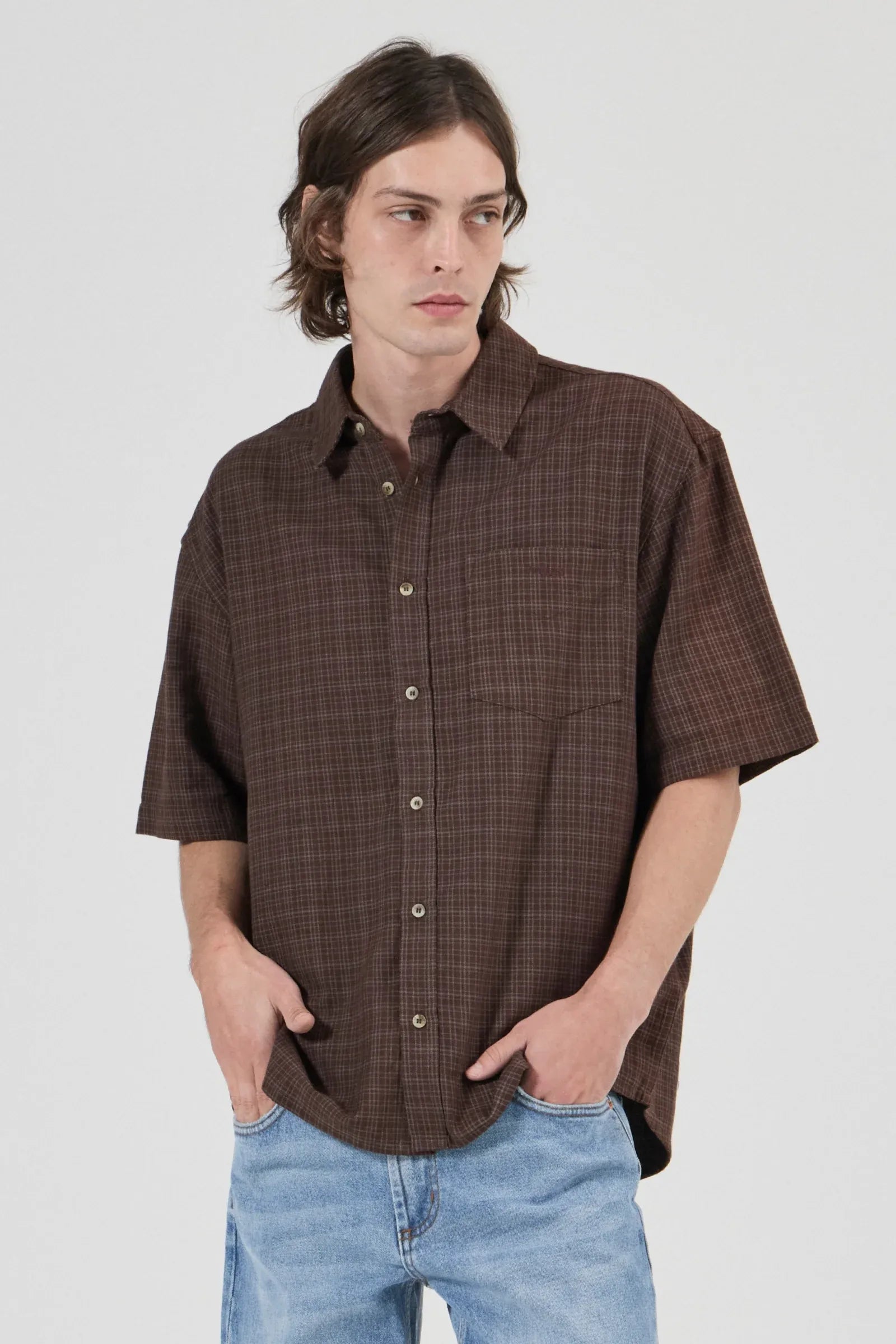 Man wearing a brown plaid shirt and blue jeans against a white background