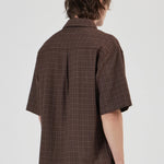 Person wearing a brown checkered shirt with short sleeves on a white background