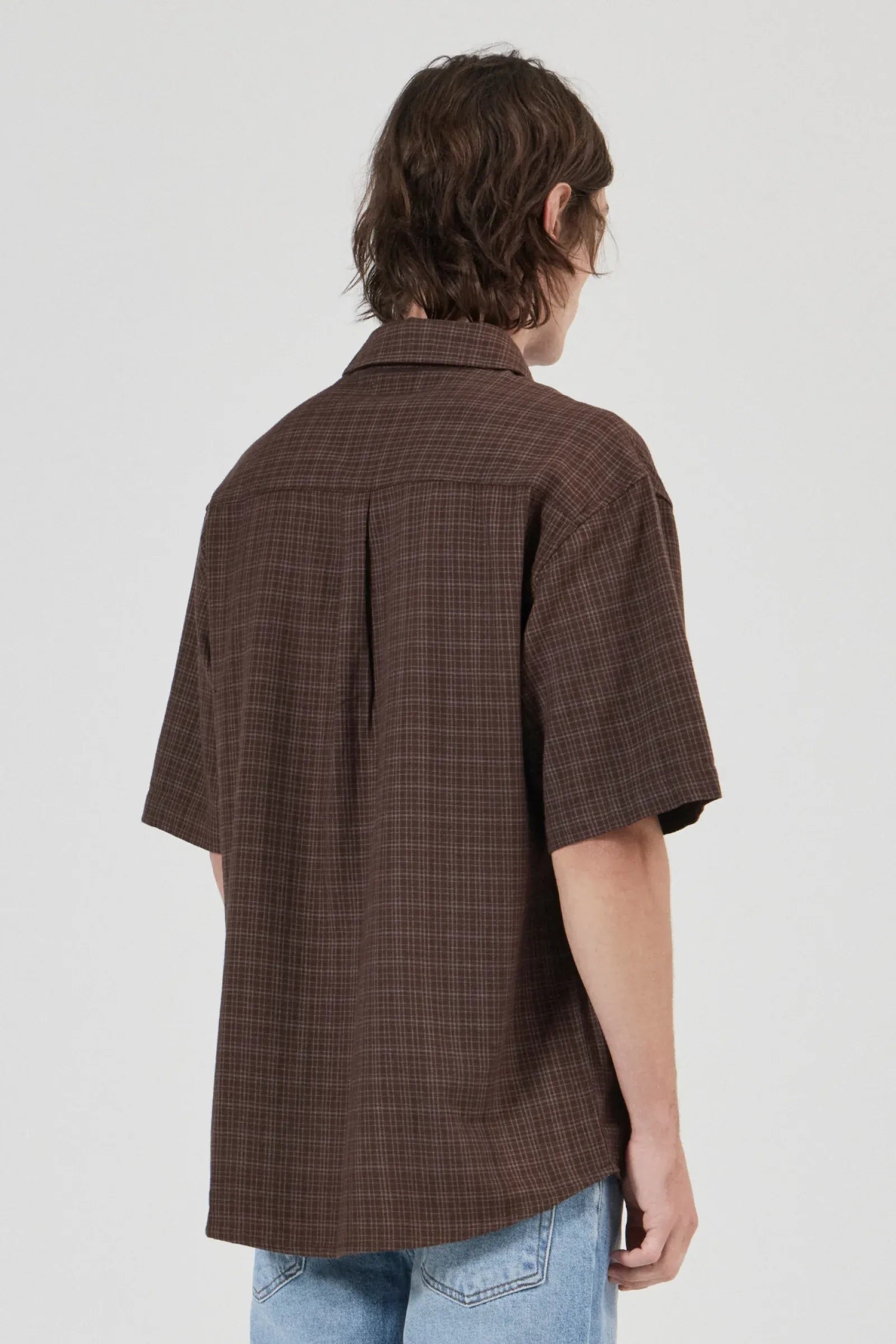 Person wearing a brown checkered shirt with short sleeves on a white background