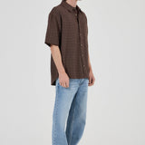 Man wearing a brown checkered shirt and blue jeans on a white background
