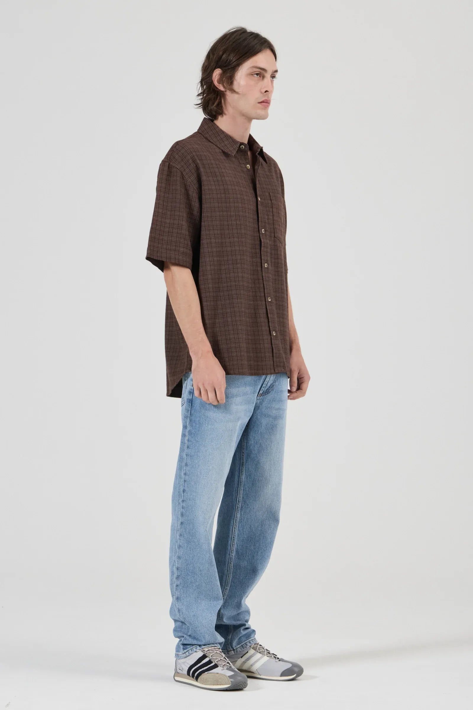 Man wearing a brown checkered shirt and blue jeans on a white background
