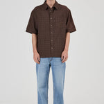 Man wearing a brown checkered shirt and light blue jeans on a white background