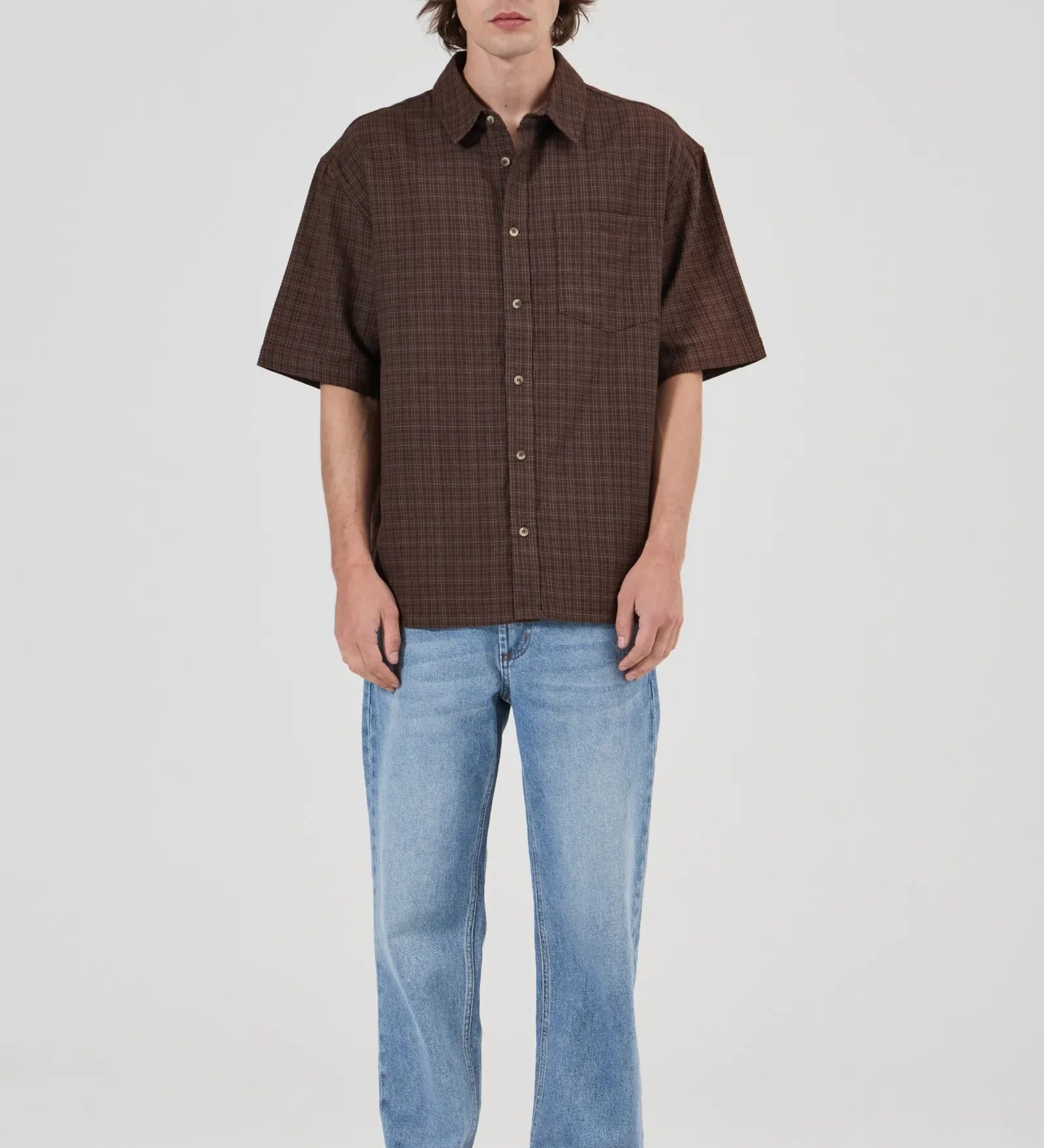Man wearing a brown checkered shirt and light blue jeans on a white background