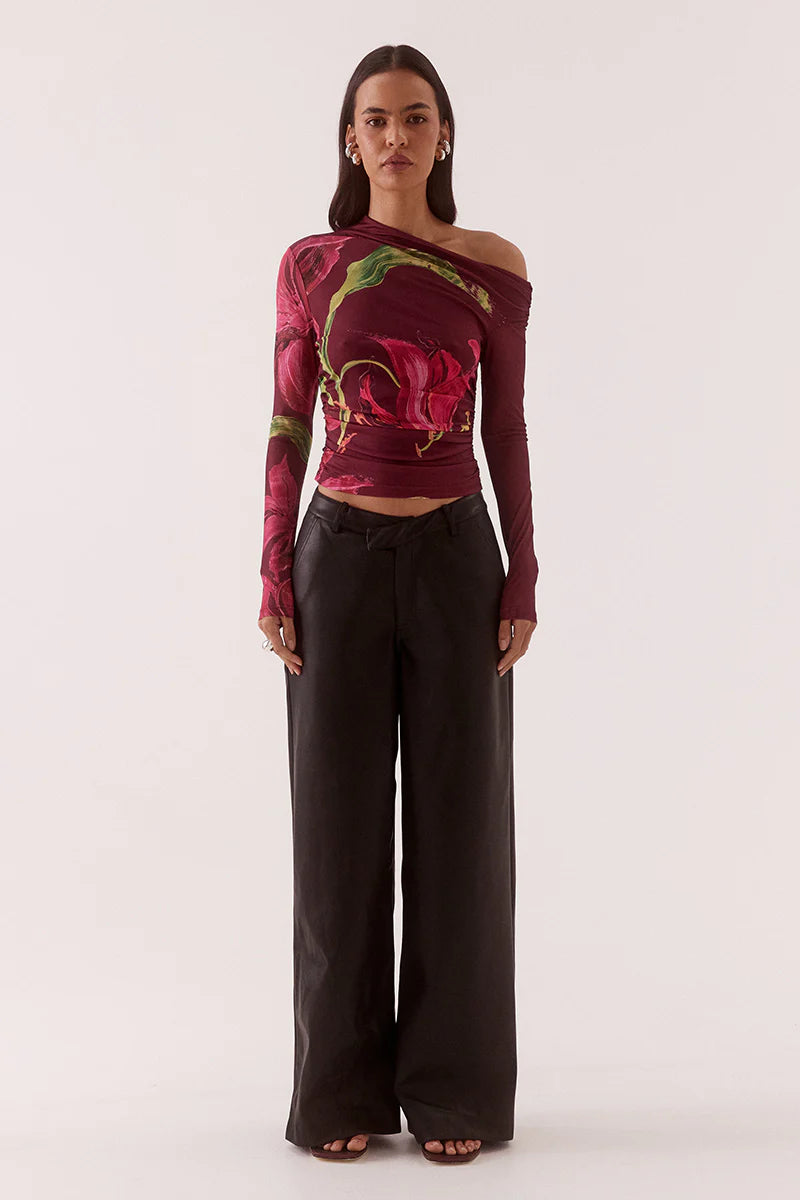 Woman wearing a colorful off-shoulder top with floral patterns and black pants on a white background